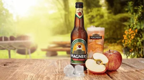 Magners original fles en glas, met ijs en appels ervoor voor een bos achtige achtergrond