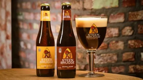 Steenbrugge flesjes, blond en brown, en een gevuld Steenbrugge glas. Staan op een tafel, bakstenen achtergrond